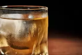 A glass tumbler with a drink and an ice cube